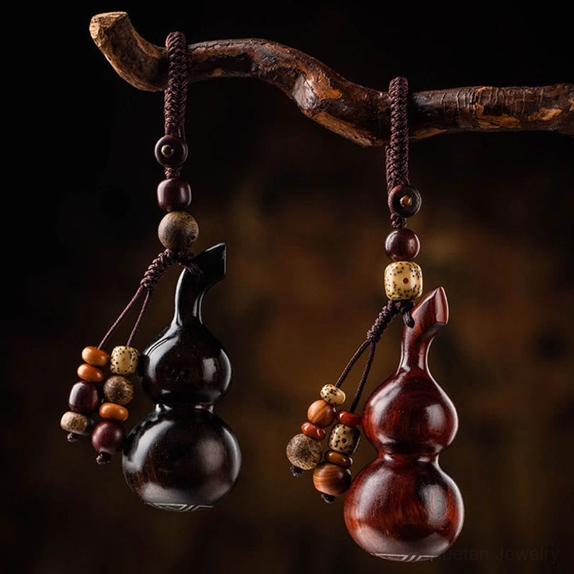 Two handcrafted gourd keychains in red sandalwood and ebony wood hung on wooden branch, side view showcasing different bead tassel styles and mixed wood colors