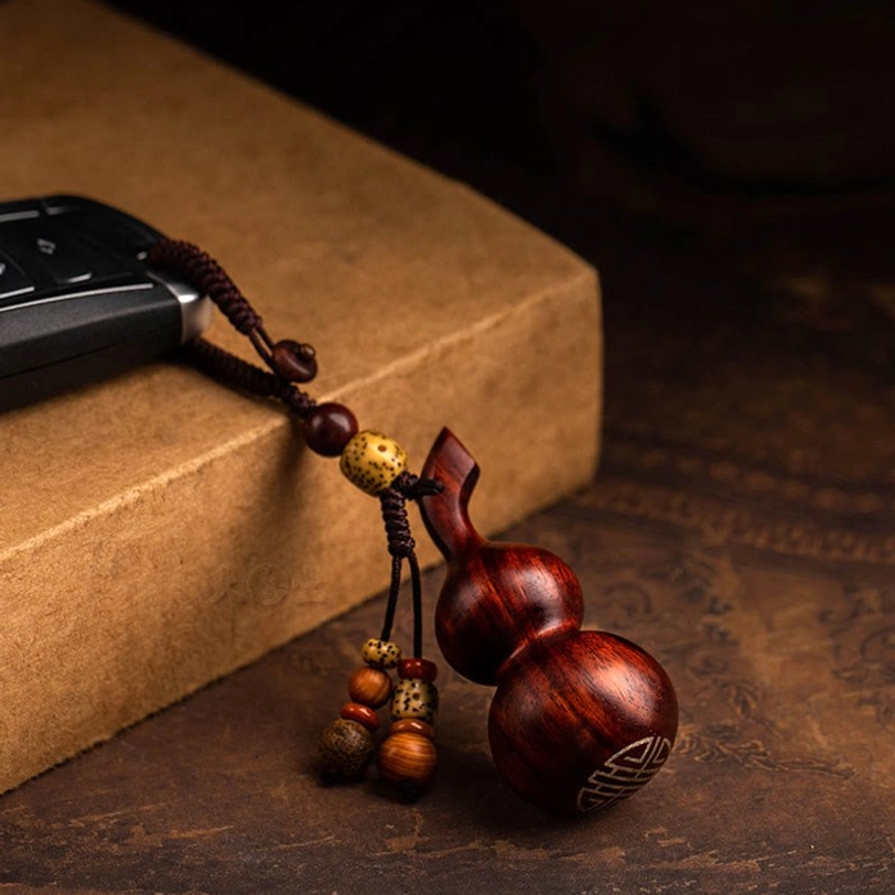 Reddish-brown sandalwood gourd keychain with engraved spiritual pattern and matching bead tassel on vintage map with wooden tray, flat lay oblique angle