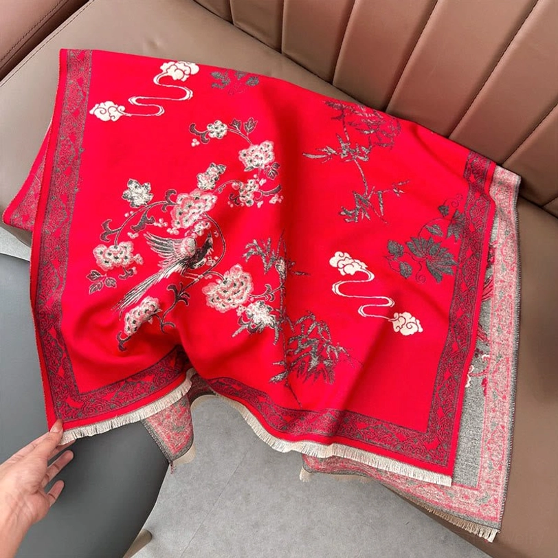 Red Tibetan jacquard scarf with bird and flower motif laid flat on sofa, decorative border with fringe
