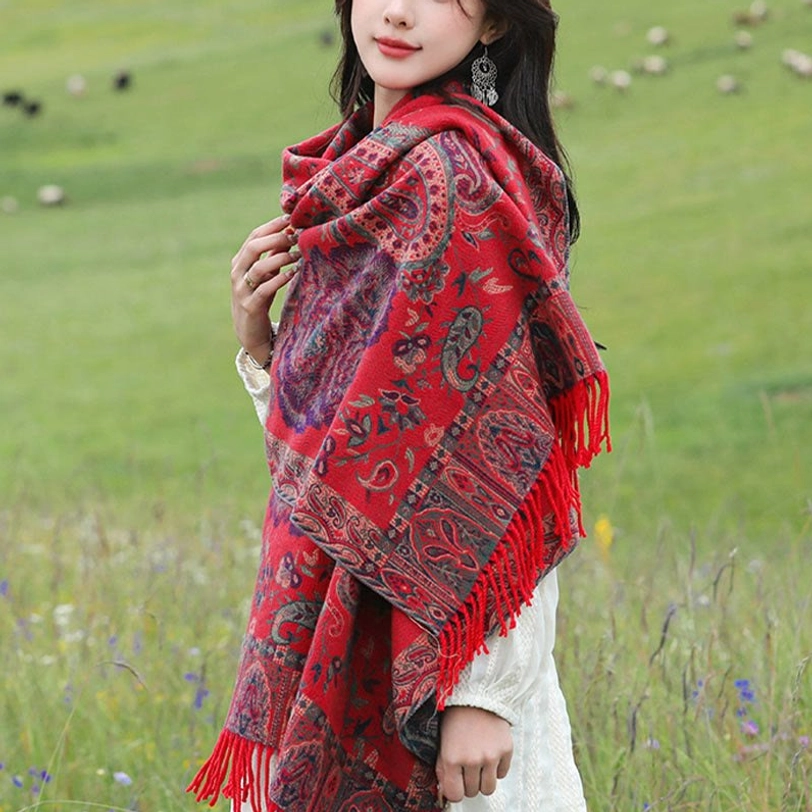 Red Tibetan shawl worn over white dress, outdoor mountain setting, vibrant paisley pattern with deep cultural meaning