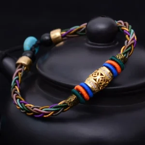 Tibetan eight knot copper coin red string bracelet handwoven close-up on black ceramic surface showing multicolor braided cord with gold and turquoise beads