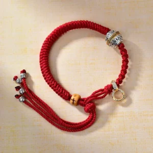Tibetan red string braided bracelet with diamond knot, carved silver bead, and gold clasp on wooden background