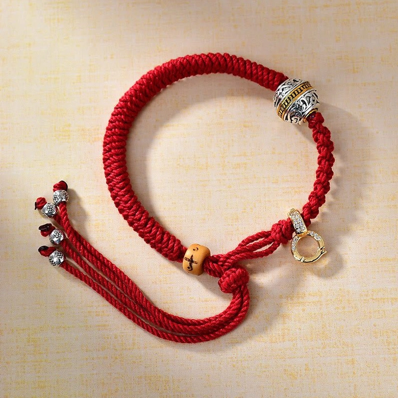 Tibetan red string braided bracelet with diamond knot, carved silver bead, and gold clasp on wooden background