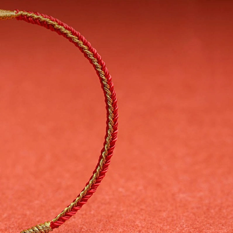 Single red and gold twisted Tibetan protection cord bracelet on matte red surface overhead view