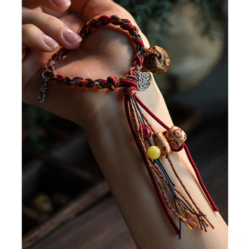 Artisan woven red cord bracelet with silver ruyi charm and ceramic bead tassel in hand close-up