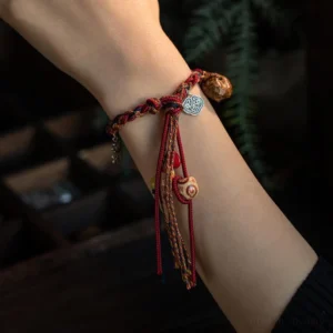 Red woven cord Tibetan protection bracelet with silver ruyi charm worn on wrist against green foliage background