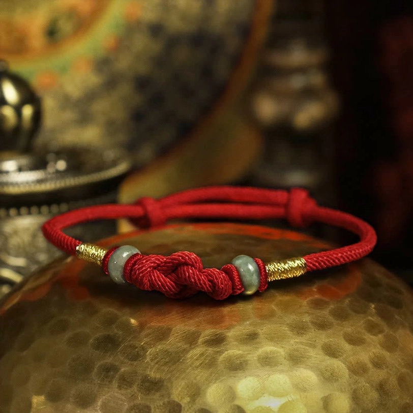 Tibetan red string bracelet with braided knot and jade beads on vintage backdrop