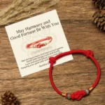 Tibetan red string jade blessing bracelet with green jade beads displayed with greeting card on wooden desk with natural pinecones