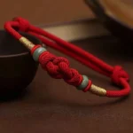 Tibetan red string jade fortune knot bracelet with gold accents overhead view on dark wooden surface