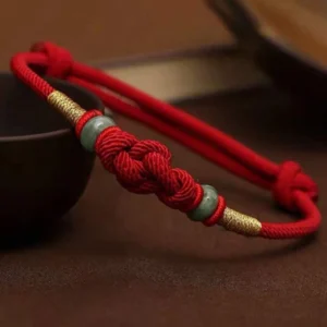 Tibetan red string jade fortune knot bracelet with gold accents overhead view on dark wooden surface