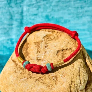 Red string jade fortune knot bracelet with gold accents displayed on natural stone