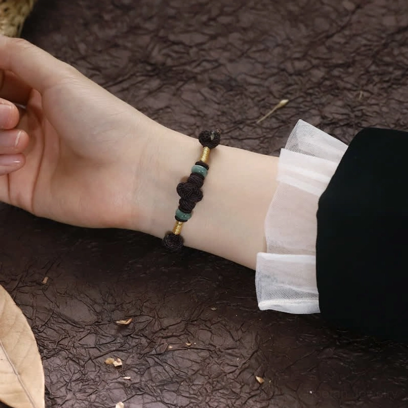 Red string jade bracelet with gold wrapped accents displaying premium craftsmanship detail
