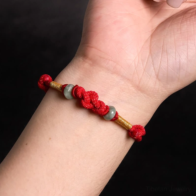 Woman wearing red string jade lucky knot bracelet on wrist against light background
