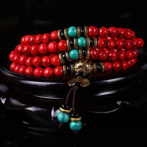 Close-up side view of Tibetan prayer bead mala necklace showing red beads with turquoise and bronze decorative details