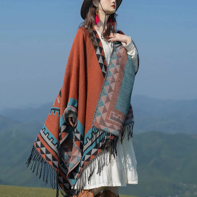 Reversible ethnic shawl worn left front three-quarter angle, displaying patterned side and tasseled hem in outdoor mountain grassland