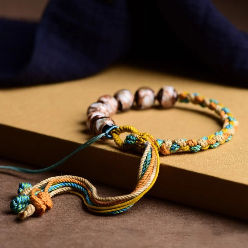 Handmade Tibetan braided fortune bracelet with long adjustable rope ends and twisted tassel, side view on kraft paper background