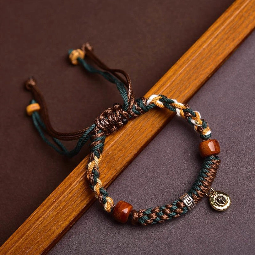 Close-up top-down view of Tibetan woven rope bracelet with brown and green braided cords, red wooden beads, and adjustable pull knots