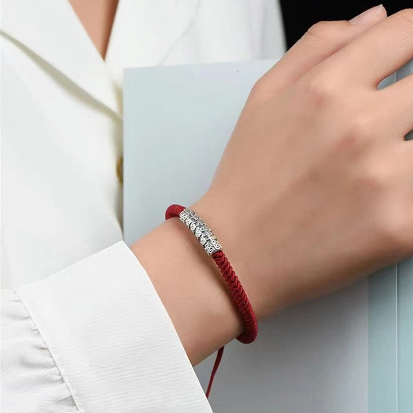 Close-up on-model shot of red Tibetan rope bracelet with detailed engraved silver charm, adjustable knot visible