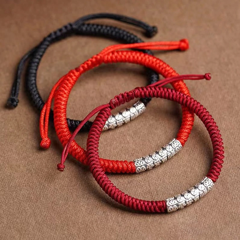 Multiple color variants of Tibetan protection rope bracelets in black and red with engraved silver charms, flat lay collection shot