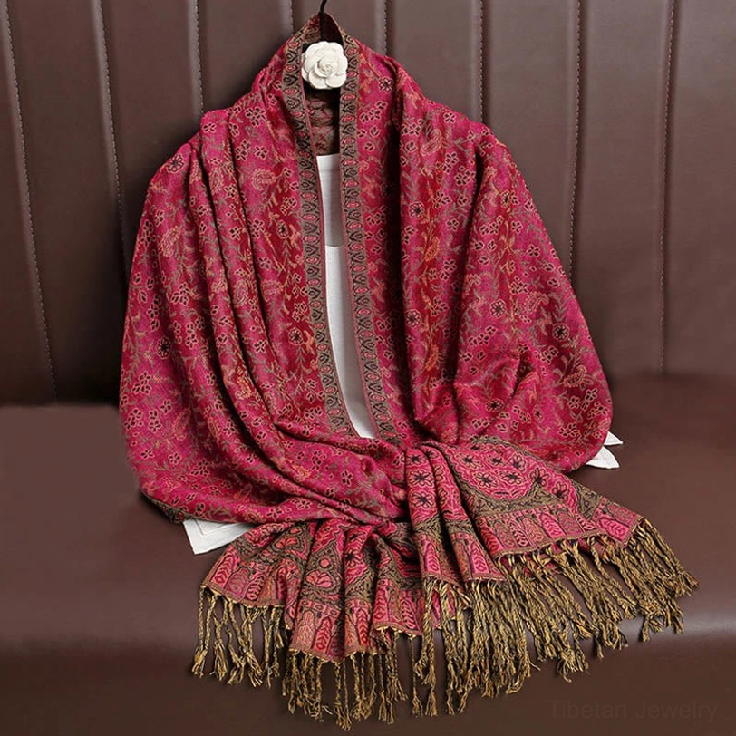 Rose red Tibetan jacquard tassel shawl with brown woven details and subtle texture, displayed on leather sofa back showing plain body with decorative fringe hem