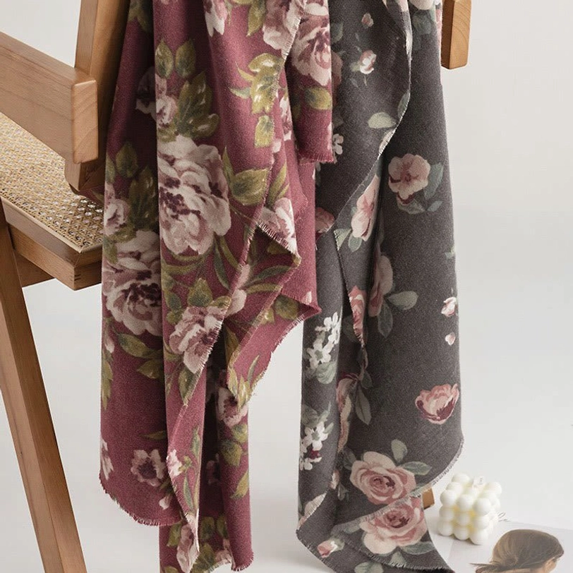 Two Tibetan garden rose shawls in burgundy and dim gray hanging display with frayed edges on rattan chair background