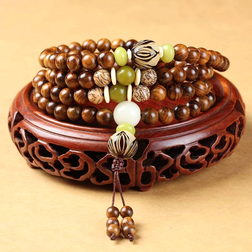Tibetan rosewood mala bracelet with 108 beads displayed overhead on carved wooden stand, showing warm brown wood beads and decorative Bodhi seed accents with tassel