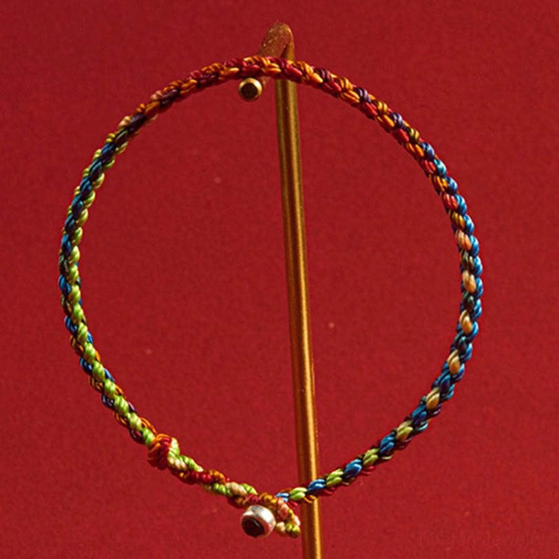 Multicolored Tibetan bracelet hanging on golden display rod with bell pendant attached