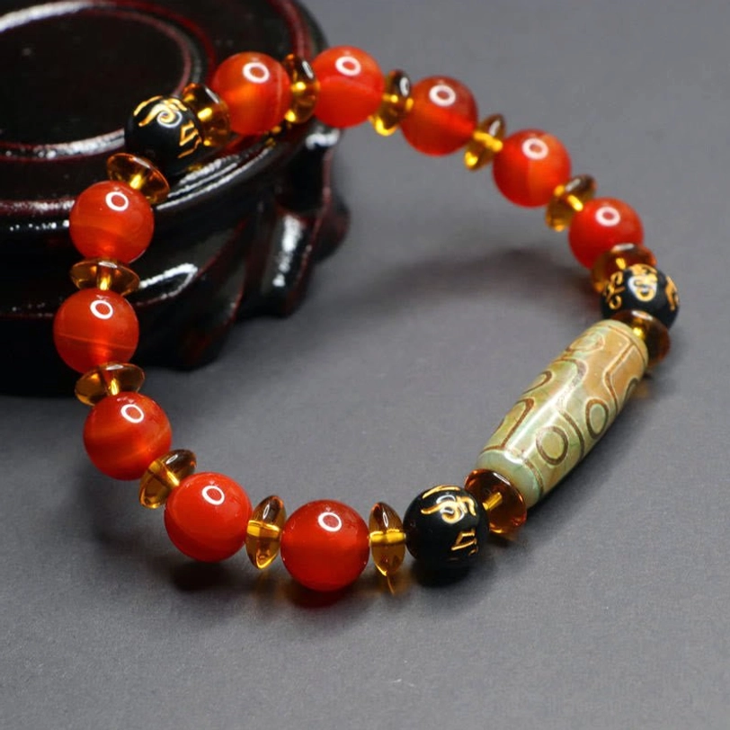 Tibetan sacred nine-eye dzi and red agate prayer bracelet styled flat lay with spiritual elements showing mantra engraved spacer beads