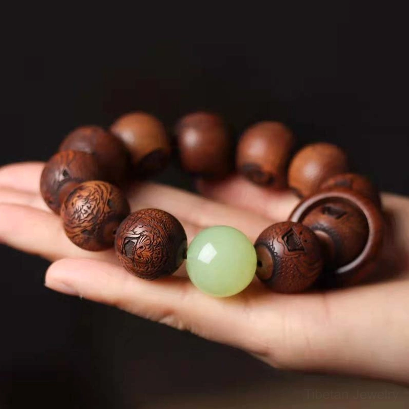 Overhead view of Tibetan sacred script engraved rosewood beads displaying fine wood texture with metal censer background