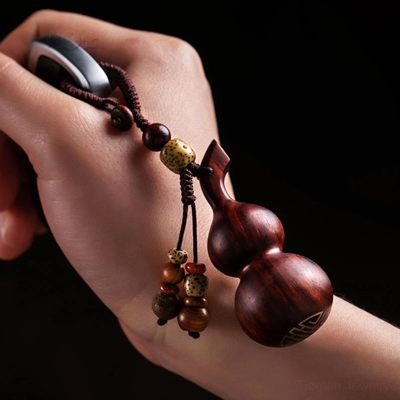 Two handcrafted gourd keychains with contrasting bead tassel styles on kraft paper box desktop, front three-quarter view displaying artisan wooden carving quality
