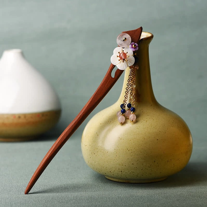 Red sandalwood hairpin with pink crystal accents and blue bead tassel beside ceramic vessel