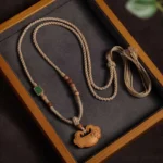 Tibetan sandalwood lock charm necklace flat lay on wooden tray showing braided cord, wooden beads, and traditional ruyi pendant
