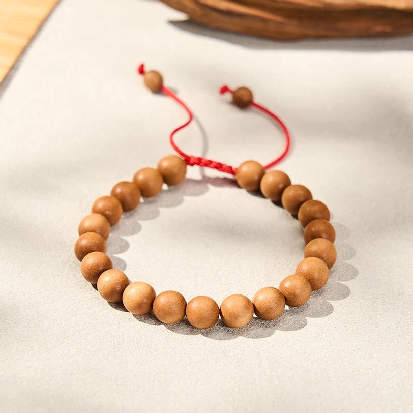 Tibetan sandalwood mala bracelet flat lay on off-white paper, showing reddish-brown beads with pendant detail