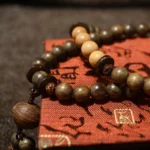 Tibetan sandalwood prayer bead mala bracelet with mixed dark and light wooden beads and decorative tassel on red patterned textile background
