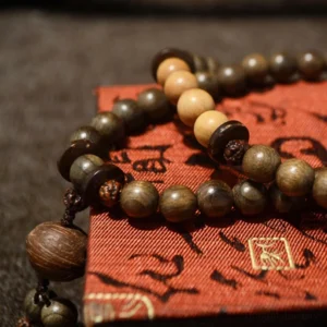 Tibetan sandalwood prayer bead mala bracelet with mixed dark and light wooden beads and decorative tassel on red patterned textile background