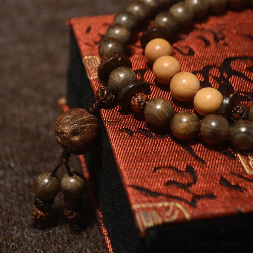 Sandalwood prayer bead mala with mixed wood tones and knotted tassel pendant on red patterned fabric background