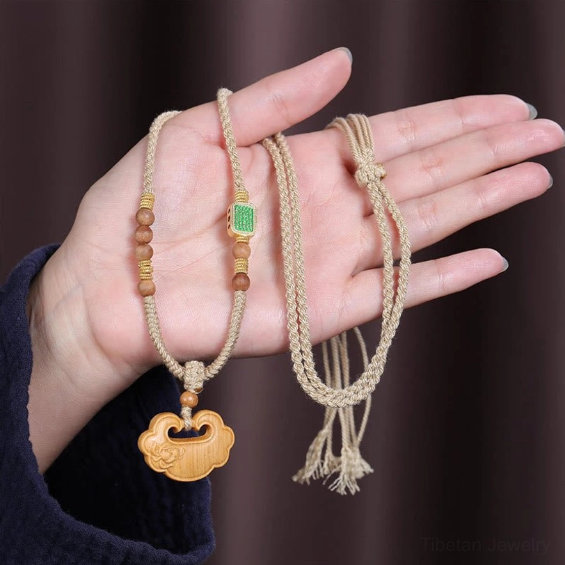 Hand holding sandalwood lock charm protection necklace displaying braided rope, tassel end, and ruyi-style wooden pendant details