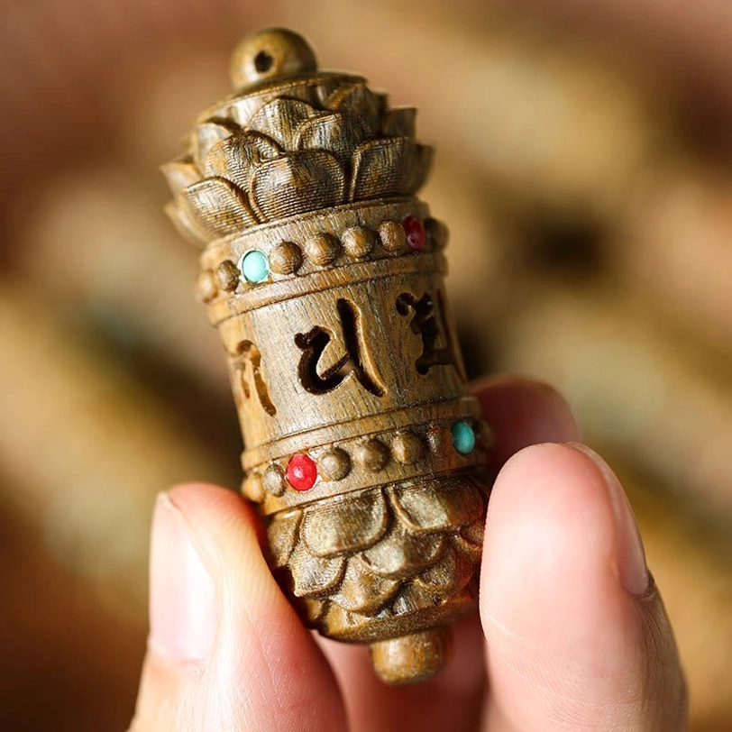 First-person view of holding Tibetan sandalwood pendant necklace between thumb and index finger, showing delicate carvings and wood texture