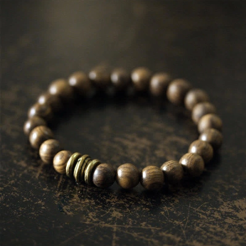 Tibetan sandalwood bracelet on dark surface, handcrafted with natural wood finish and traditional bronze spacer rings for spiritual wellness