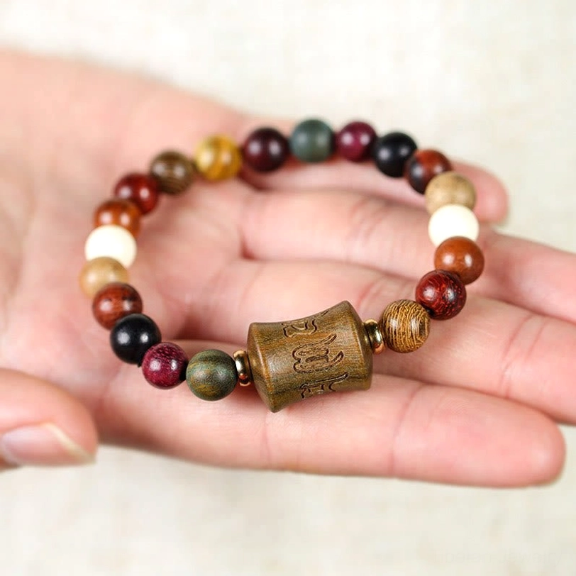 Handmade Tibetan sandalwood bracelet with carved Om Mani Padme Hum focal bead held in fingers against light background