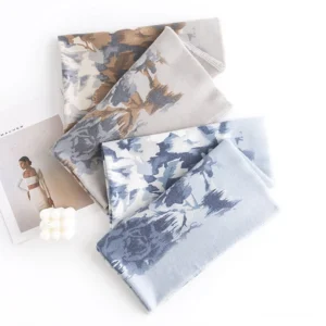 Multiple folded Tibetan scarves in brown and blue-white floral designs arranged in flat lay with fashion magazine and candle for cozy home styling