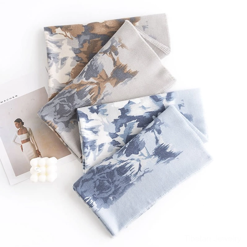 Multiple folded Tibetan scarves in brown and blue-white floral designs arranged in flat lay with fashion magazine and candle for cozy home styling