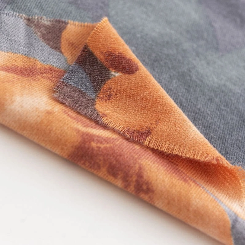 Corner detail of Tibetan floral scarf with frayed fabric edge and warm orange hibiscus pattern