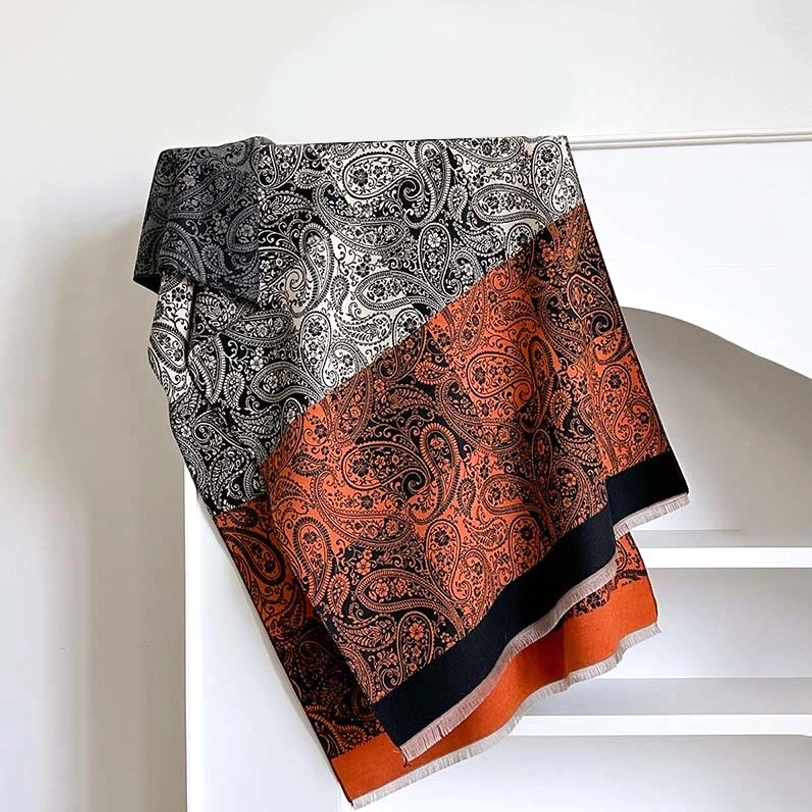Dark orange Tibetan scarf with paisley vine pattern, displaying burnt orange and brown tones with black hem trim on shelf