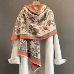 Tibetan floral bird printed scarf shawl in orange-red beige draped over white coat, front view studio photo
