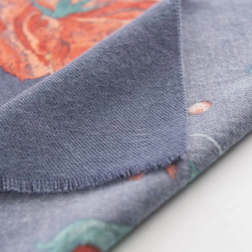 Tibetan scarf edge detail showing raw frayed hem finish on muted blue-gray base with partial floral print visible