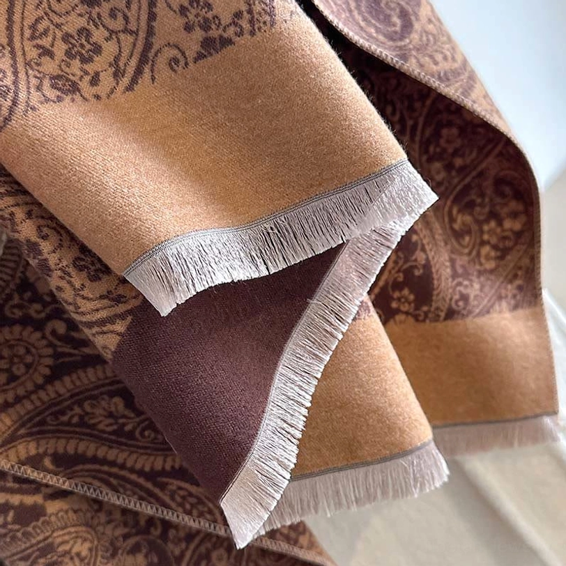 Close-up detail of Tibetan winter scarf showing frayed tassel hem edge, woven texture, and multi-tone block paisley design