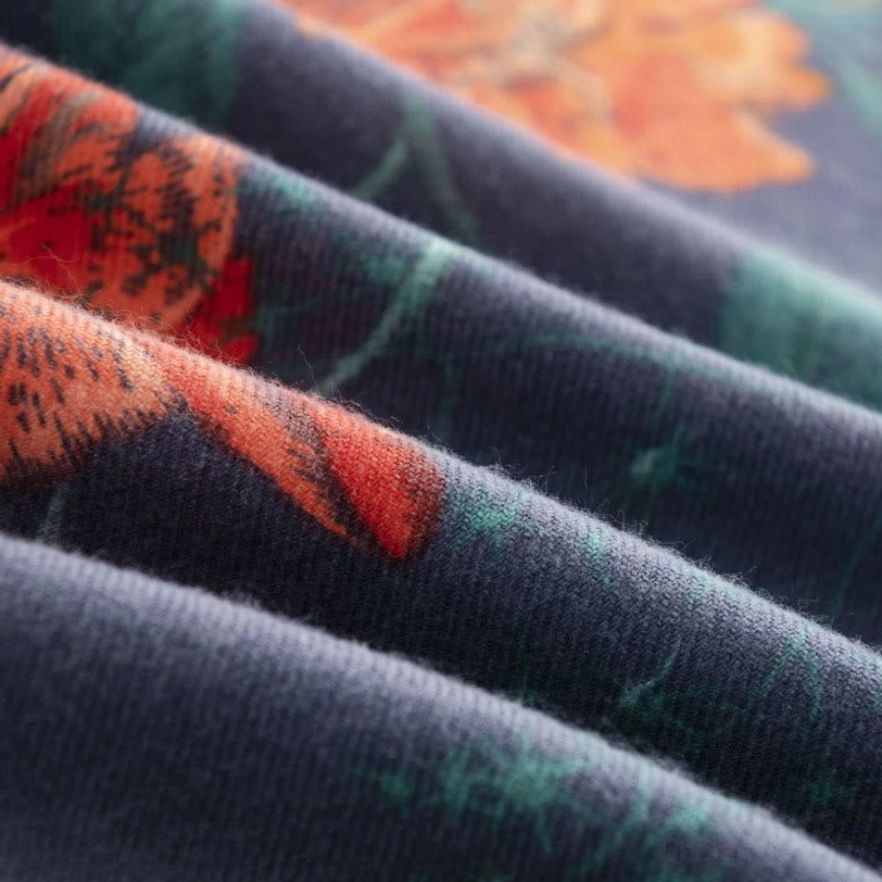 Soft folded Tibetan scarf fabric showing warm-toned floral botanical prints on navy base with low angle close-up view