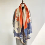 Tibetan landscape floral scarf in warm autumn tones worn as elegant shoulder wrap on mannequin with minimalist studio background