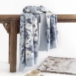 Tibetan floral scarf wrap with blue-white abstract pattern displayed on vintage wooden table, side angle view showing soft woven fabric texture